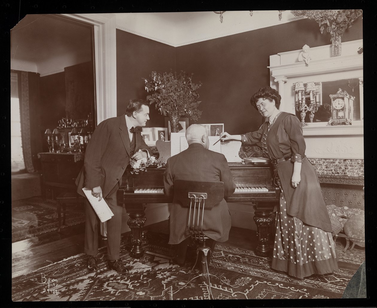 Clara De Regand, bir adam piyano çalarken bir notayı işaret ediyor, 1910 (gümüş jelatin baskı) by Byron Company