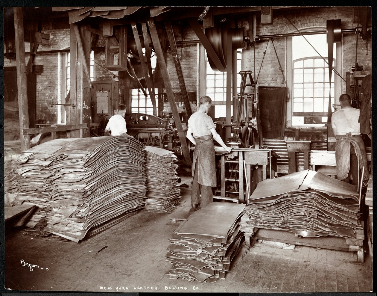 Interior view of three men working with leather and heavy equipment at the New York Leather Belting Co., New York, 1905 (silver gelatin print) by Byron Company