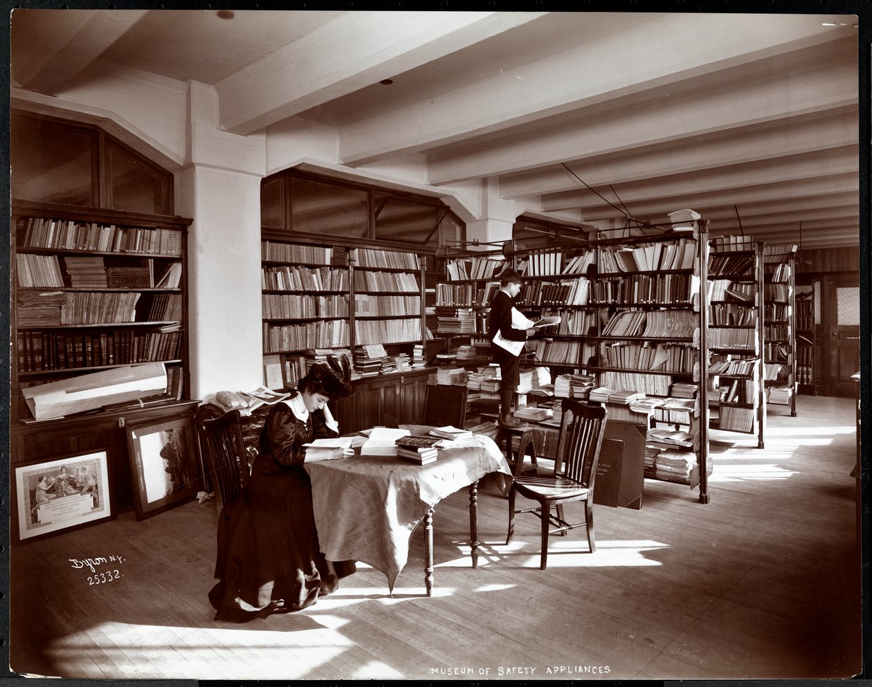 Amerikan Sosyal Hizmet Enstitüsü'nün Güvenlik Aletleri Müzesi'nin bir kütüphanesindeki kadın ve genç bir adam, New York, 1907 (gümüş jelatin baskı) by Byron Company