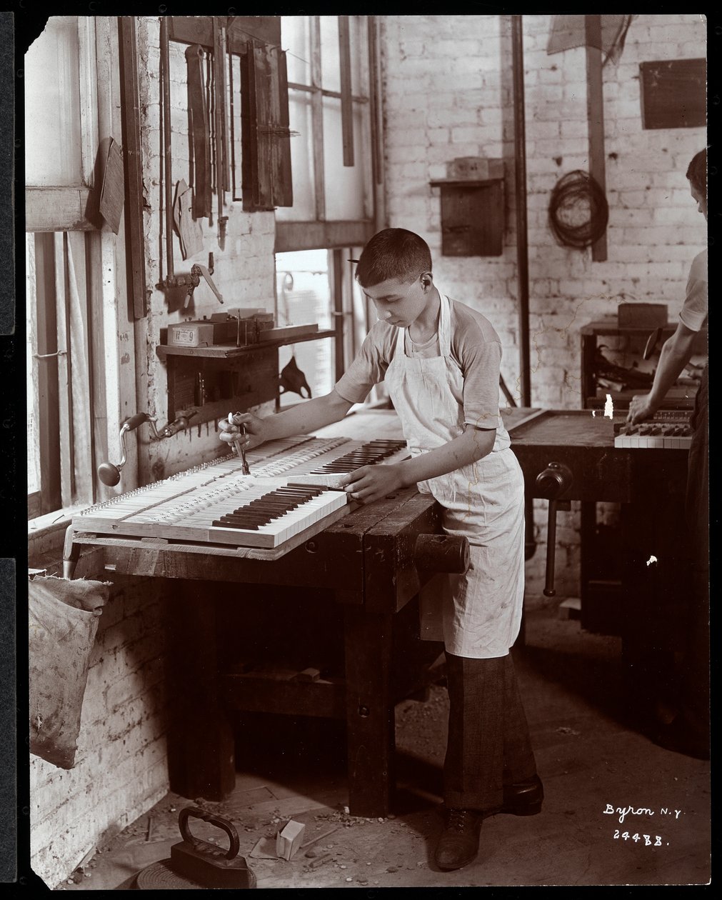Harrington Piano Co. fabrikasında çalışan genç bir adam, 1907 (gümüş jelatin baskı) by Byron Company