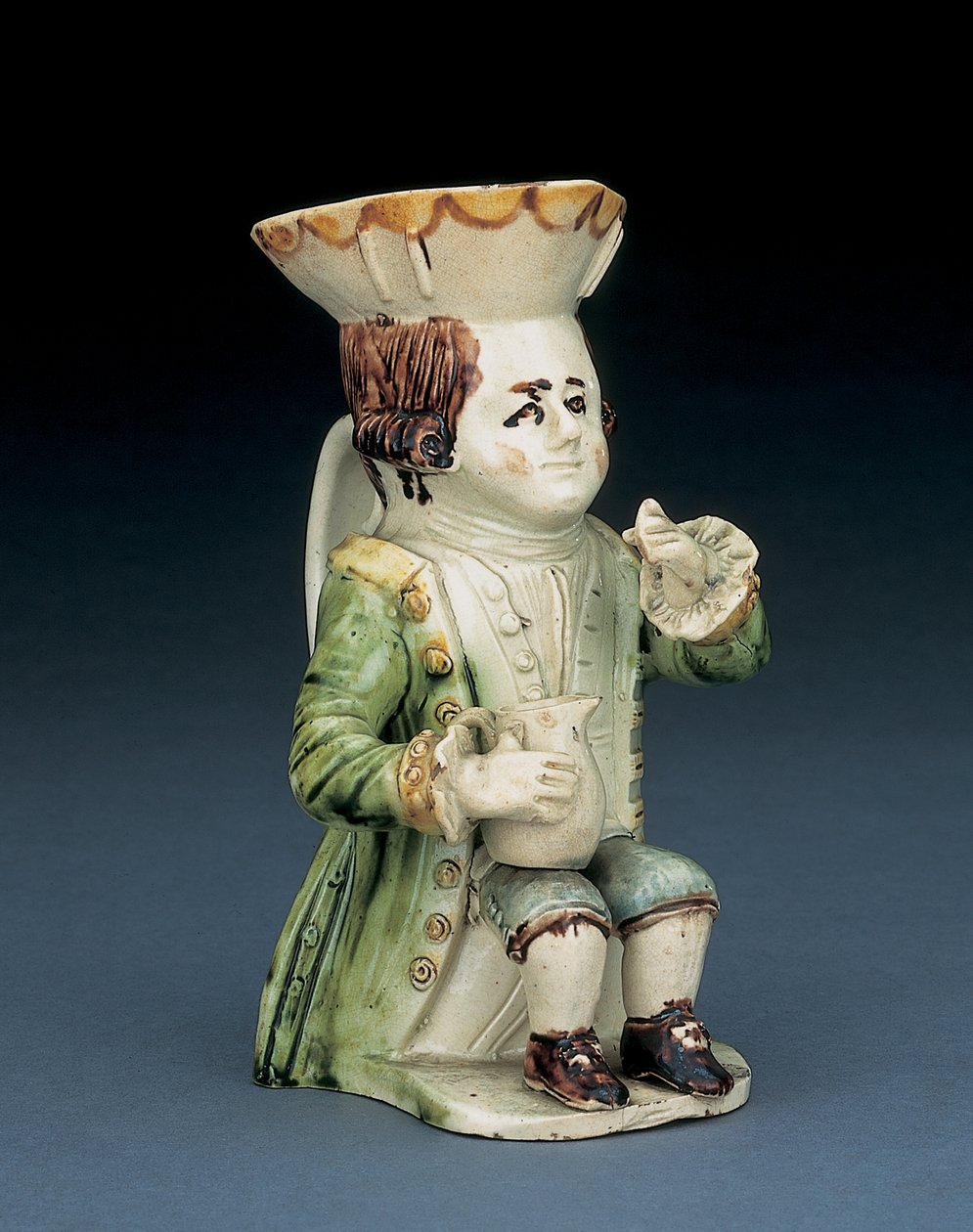 Toper toby sürahisi, kenarları kahverengi ve sarı dalgalı şapkası, sıraya kazınmış kahverengi saçları ve dizinde korkuluklu bir sürahi ile oturan beyaz bir rozet, c.1770 by English School