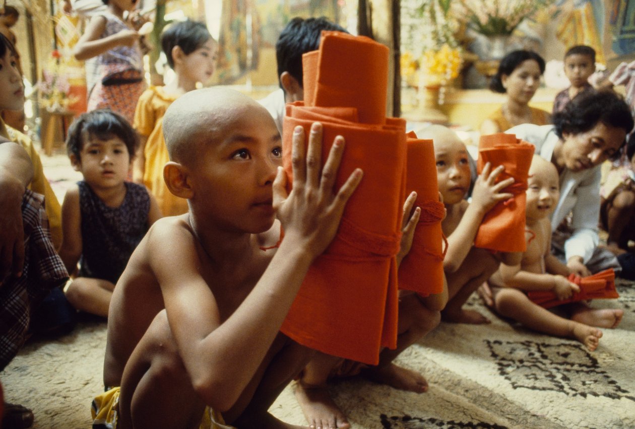 Kafası tıraşlı genç bir çocuk keşiş kıyafetlerini alıyor. Mandalay, Burma. by James L Stanfield