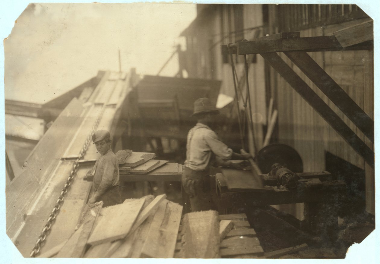 Charlie McBride aged 12 takes wood from a chute for 10 hours at Miller und Vidor Lumber Company, Beaumont, Texas for which he earns 50 cents while the other boy saws it on an unguarded circular saw, 191 by Lewis Wickes Hine