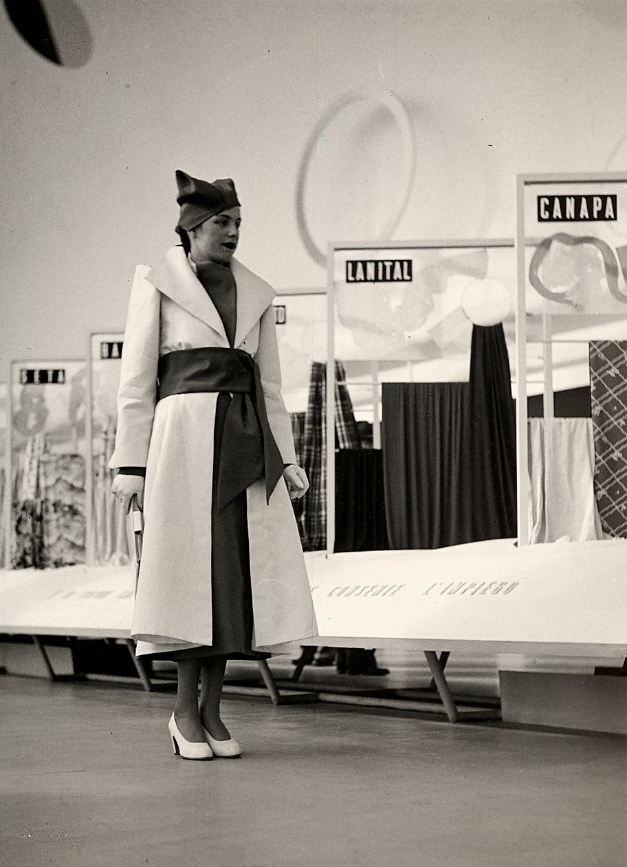 Couture evi "Lamma" tarafından oluşturulan bir paltoda model. Ürün, geniş bir kuşakla belden toplanmış ve yumuşak bir şapka ile tamamlanmıştır. Fotoğraf, kumaş sergisi için kullanılan bir salonda çekildi. (s/b fotoğraf) by Luis Bogino