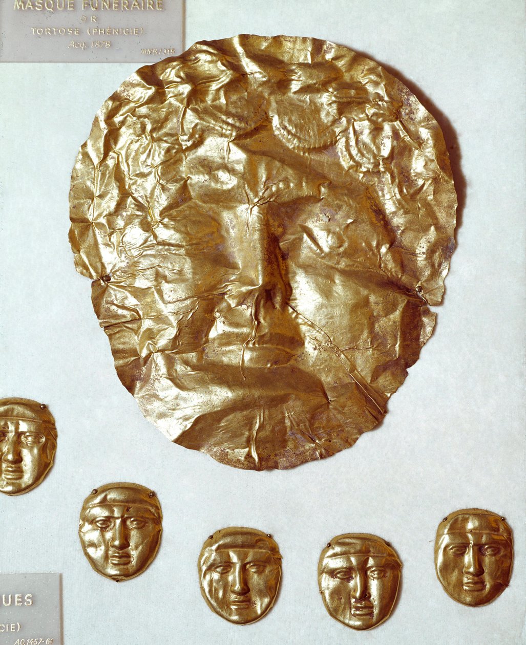 Fenike sanatı: kadının yüzünde büyük altın varak maskesi ve aşağıda beş küçük altın maske grubu by Phoenician Phoenician