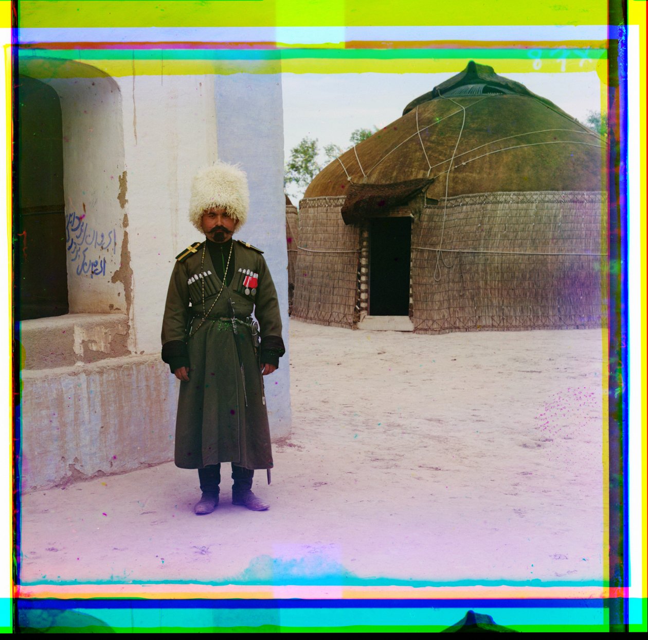 Üniformalı silahlı bir adam, arka planda yurt olan bir binanın yanında duruyor, Rusya, 1915 by Sergey Prokudin Gorsky