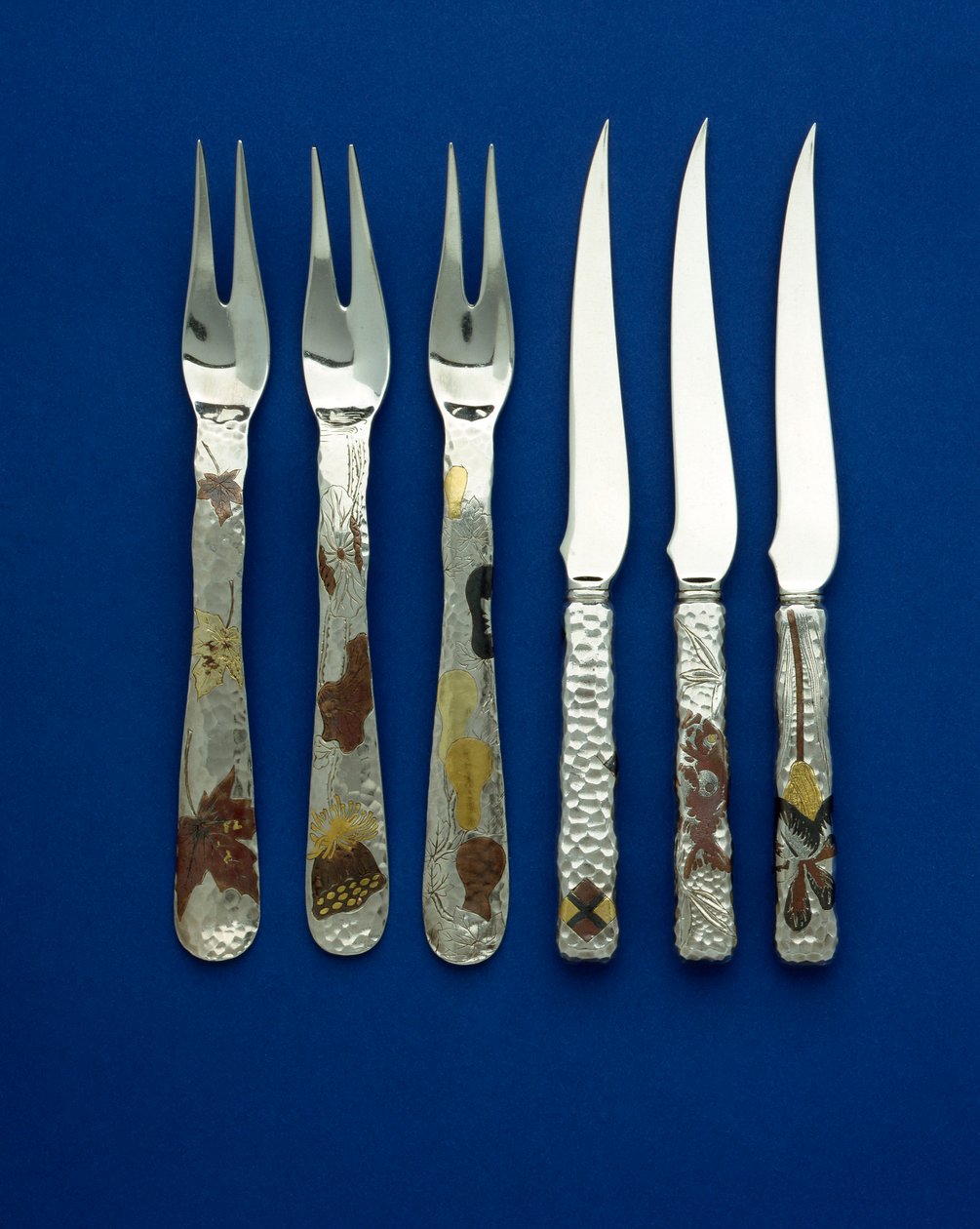 36 tatlı bıçak ve çataldan oluşan zarif ve nadir bir setin parçası, çeşitli çiçek, hayvan ve geometrik desenlerin oyulmuş detayları ile patinalı bakır ve vari renkli altın işlemeli spot dövme saplar, c.1880 (bakır, altın) by Tiffany and Company