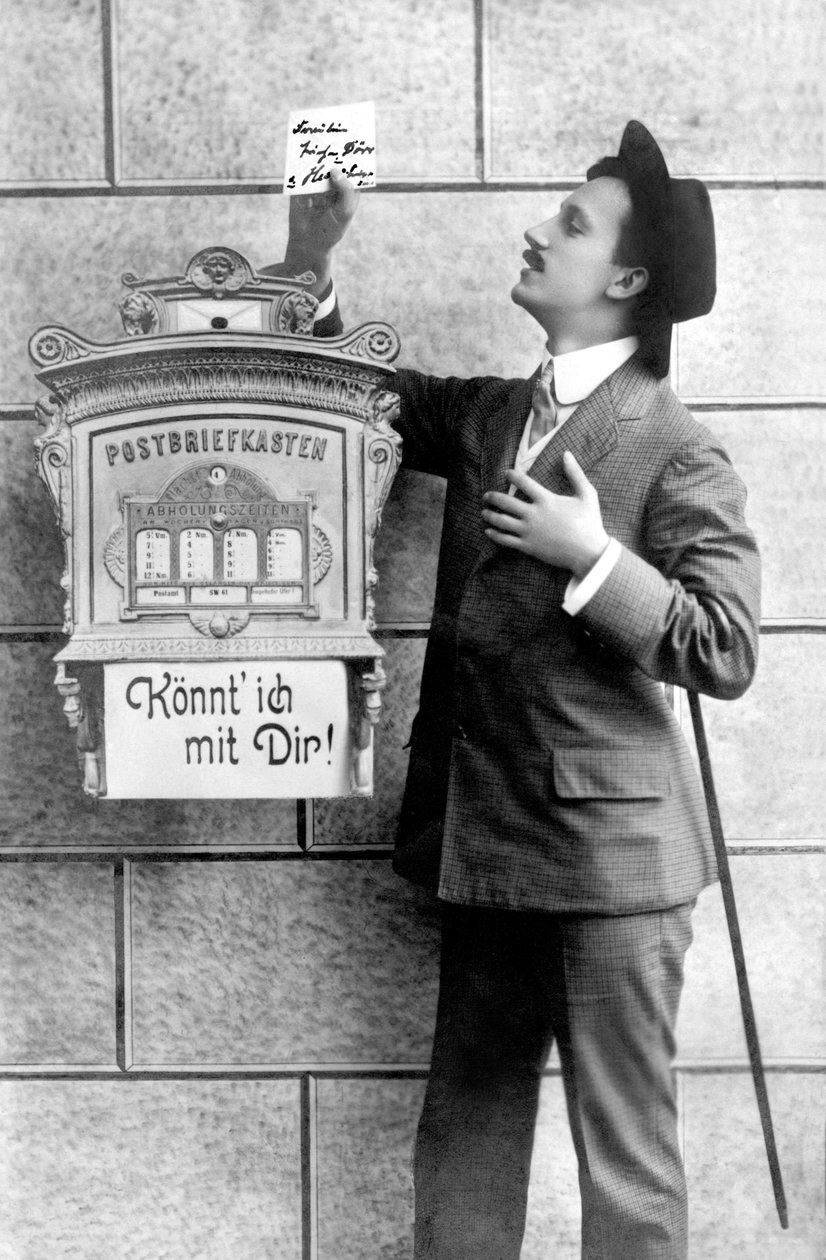 Takım elbiseli, şapkalı ve bastonlu zarif bir adam posta kutusuna bir not gönderir. 1920 civarında Almanya Tarihi fotoğraf, bir mektup kutusunun yanındaki adam, 1920 civarında by Unbekannt