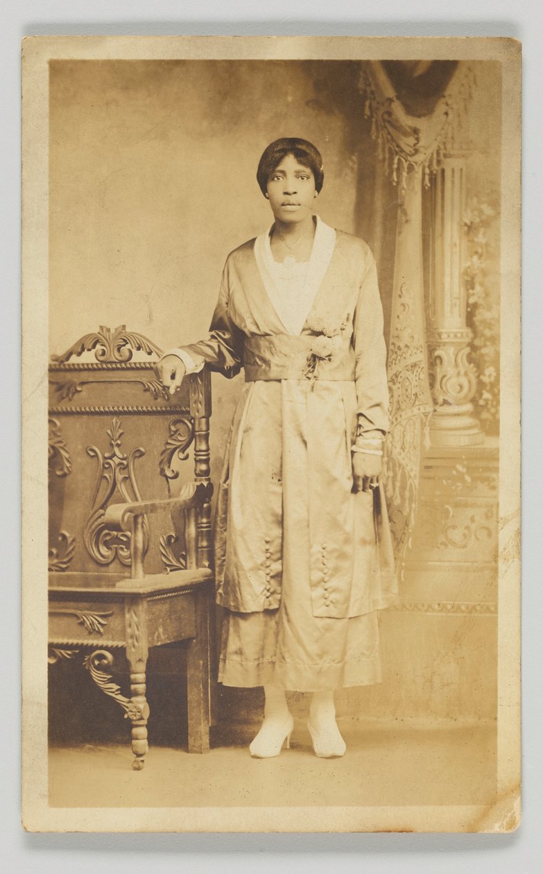 Ahşap bir sandalyenin yanında duran bir kadının fotoğrafik kartpostalı, 1904-1918. by Unbekannt