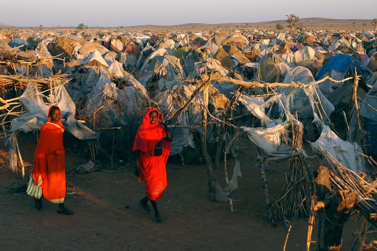 Parlak kırmızı giysiler giyen kadınlar, Ülke İçinde Yerinden Edilmiş İnsanlar için Otash kampında yürüyor by Unbekannt Unbekannt