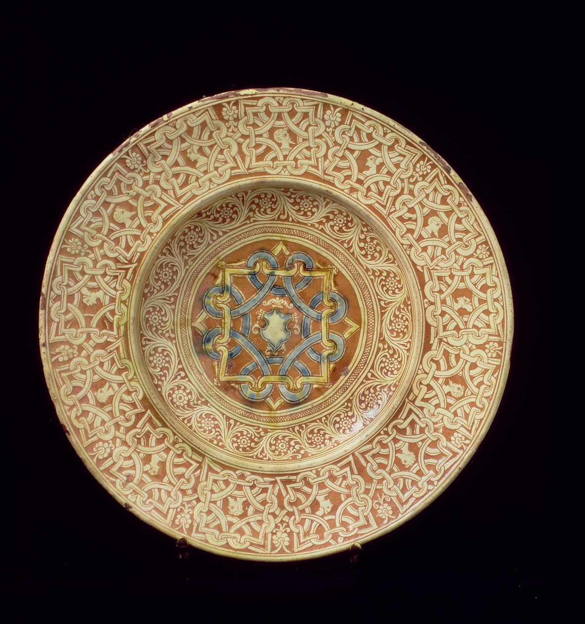 Maiolica plakası, bordürde profil başlarını çerçeveleyen ayrıntılı bir tekrarlayan düğüm tasarımlı çerçeve ve merkezi plakada bir kalkan ile dekore edilmiştir, İtalyan, Toskana