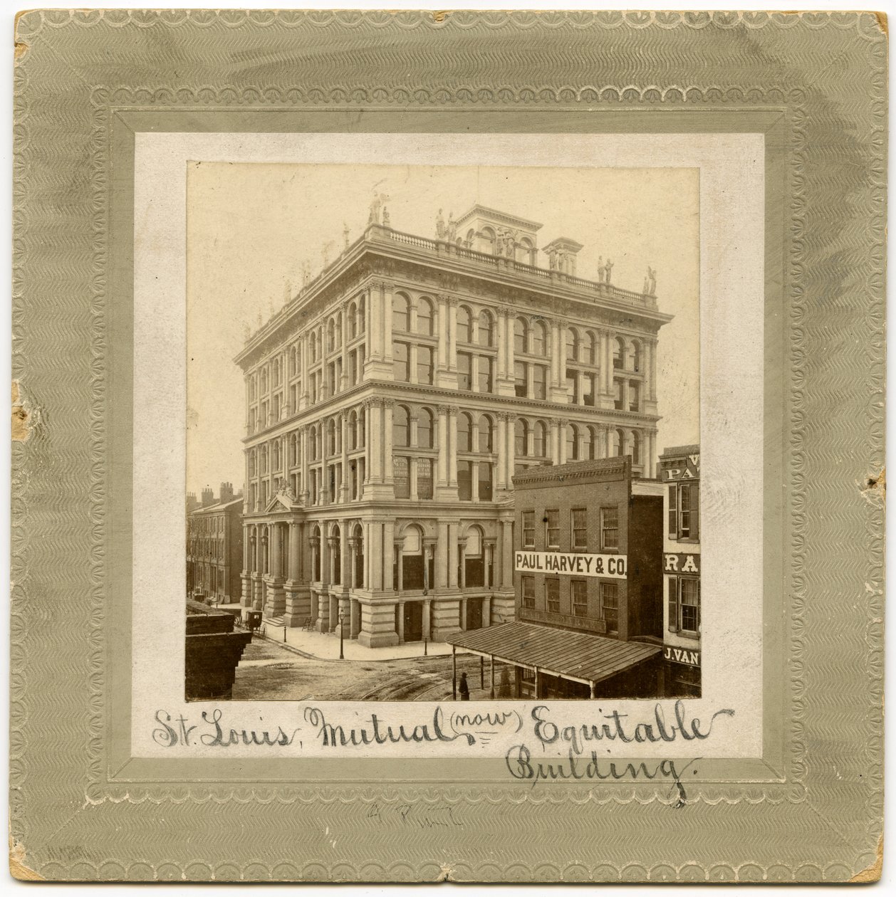 Üstte figürler bulunan altı katlı bir binanın fotoğrafı. Her iki tarafta da görünen başka binalar var. St. Louis Hayat Sigortası Binası olarak da adlandırılan bina by Unknown