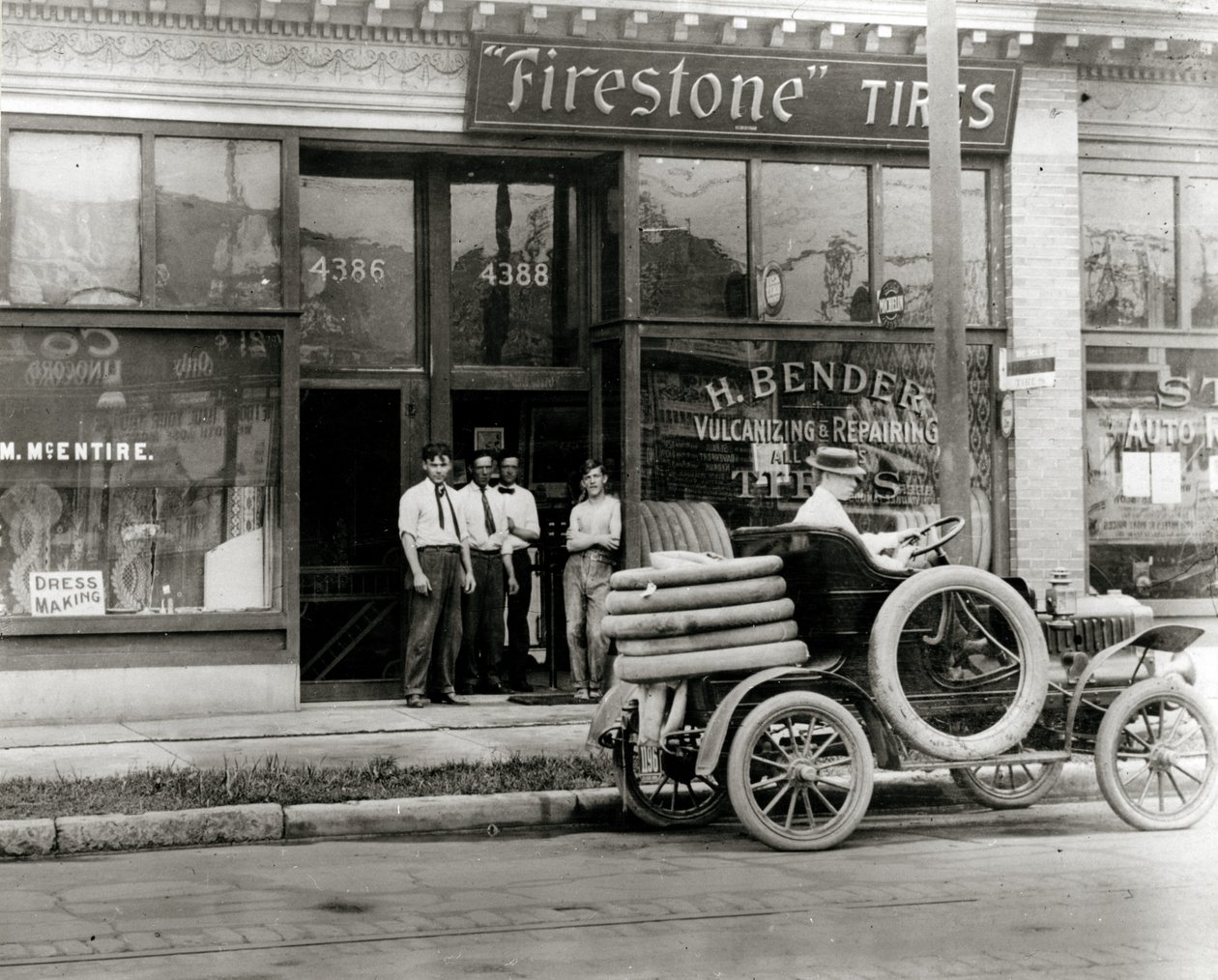 4388 Olive Street adresindeki H. Bender Firestone Tire bayisinin önünde toplanan erkekler ve otomobil lastik tamircisi by Unknown