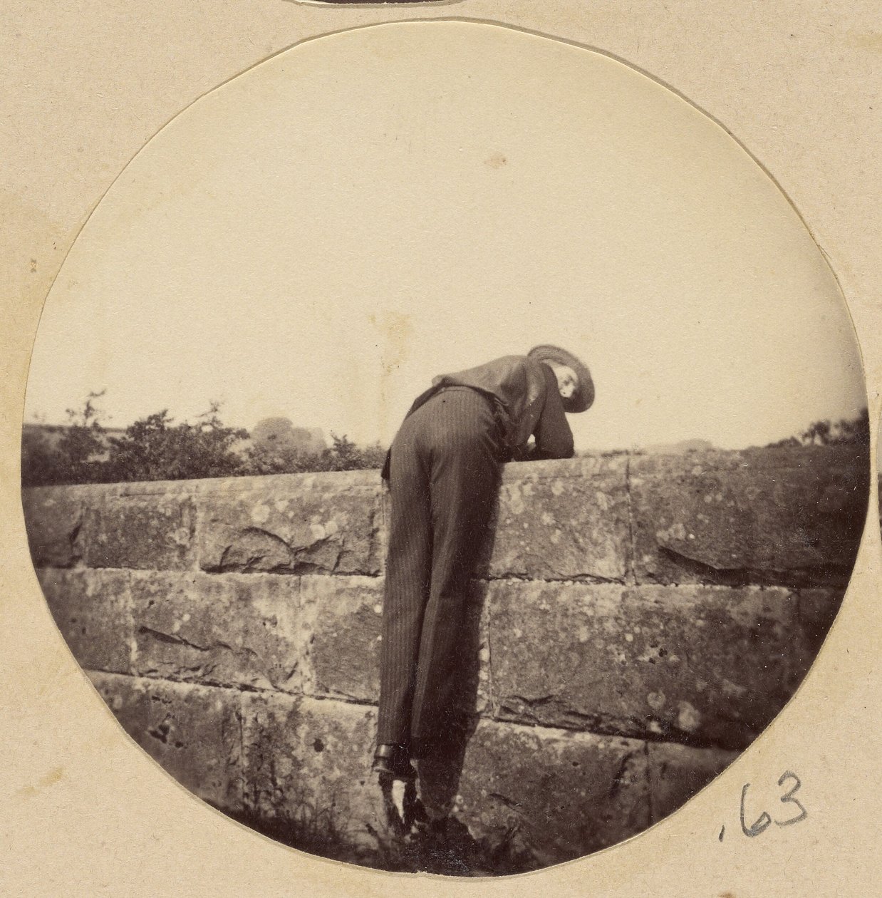 [Şapkalı adam taş bir duvarın üzerine eğildi] by Unknown artist