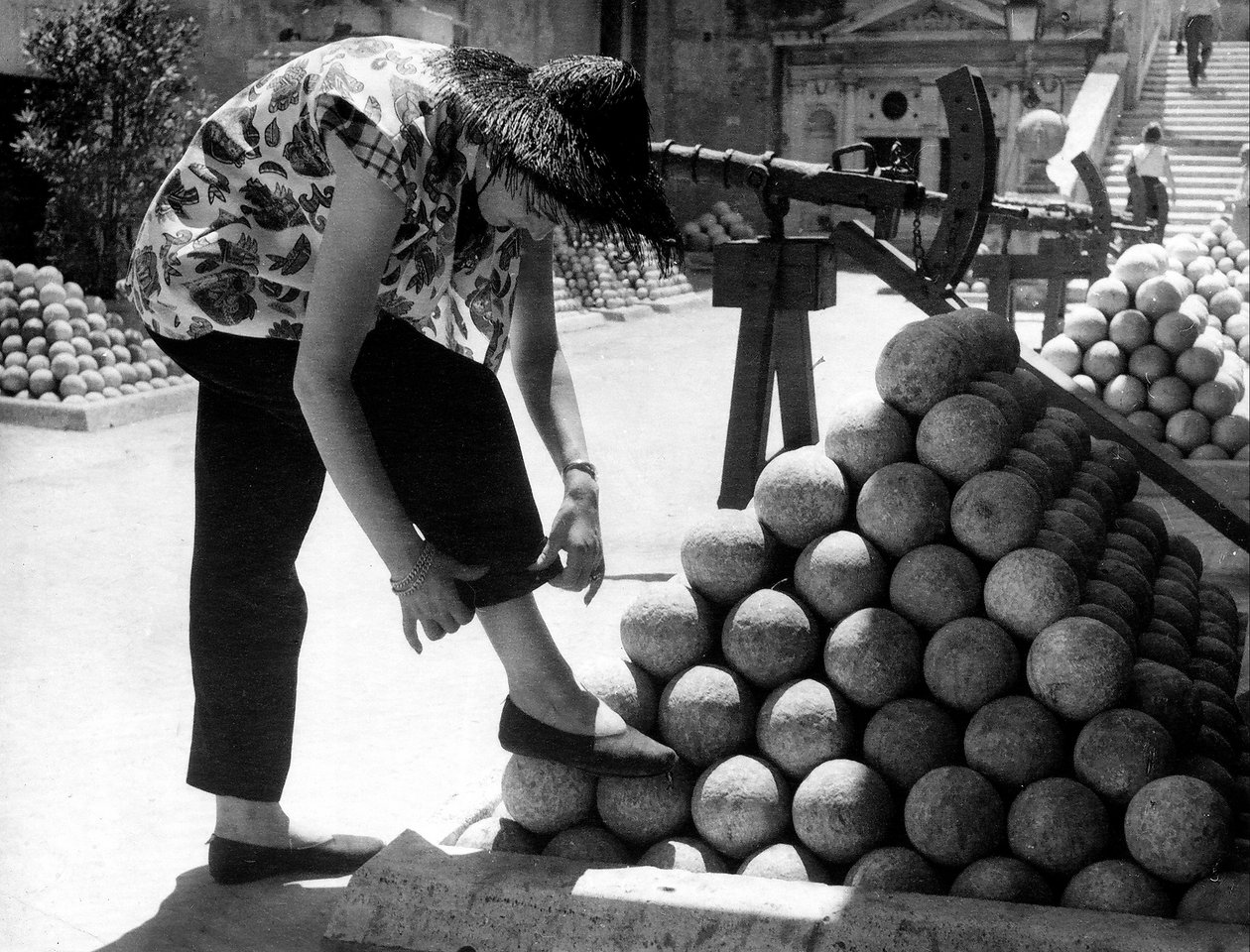 Bir kadın, Roma#39;daki Castel Sant#39;Angelo arazisindeki gülle yığınının üzerine ayağını koyarken pantolonunun manşetini düzeltiyor. by Unknown photographer