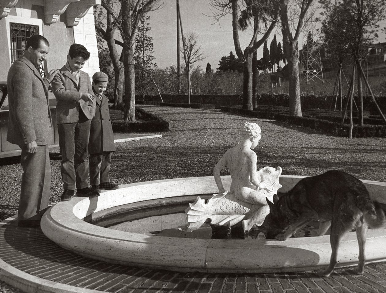 Gino Bartali, iki çocuğu ve bir köpeğiyle çeşmenin yanında by Unknown photographer