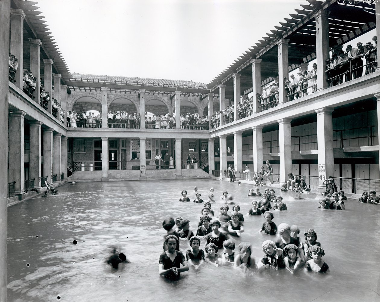 Sütunlarla desteklenen iki katlı balkonlu bir yüzme havuzunun yatay, siyah beyaz fotoğrafı. Seyirciler ikinci kat balkonundan yüzücüleri izliyor by William G. Swekosky