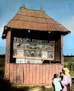 Romanya, Bukovina, Azizlerin resimlerinin bulunduğu küçük bir şapelin önünde çocuklu anne, resim tarihi: 1920 civarı. Carl Simon Arşivi by Carl Simon