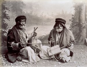 Mütevazı etnik elbiseli iki Arap müzisyenin portresi. Yaşlı adamlar yerde oturmuş stüdyoda poz veriyorlar. Arkalarında ormanlık bir manzara fonu var. by Félix Bonfils
