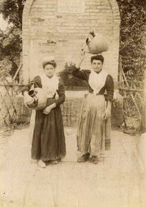 Geleneksel kıyafetler giyen ve kuyu başında pişmiş toprak küpler taşıyan iki genç kadın, Marche, İtalya, 1910 civarı by Italian Photographer