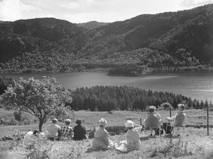 Çimlerde veya şezlonglarda oturmuş Thirlmere manzarasına bakan bir grup insan by Joseph Hardman