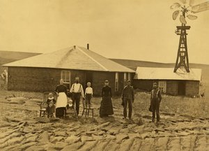 Nebraska, Custer County'deki bitişik binanın çatısında bir yel değirmeni olan çim evlerinin dışında çiftçi ailesi, 1885 dolayları (s/b fotoğraf) by Solomon D. Butcher