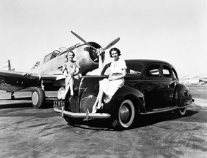 California: 1939 İki kadın, arkalarında tek motorlu bir uçak park etmiş bir havaalanında 1939 model Lincoln Zephyr sedanın çamurluklarında oturuyor (s/b fotoğraf) by Unbekannt