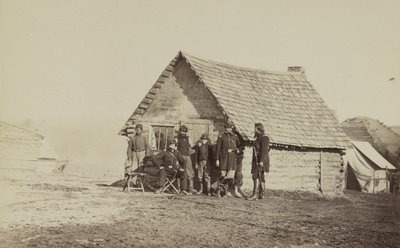 Bir grup asker ve biri Afrika kökenli Amerikalı iki genç adam, kütüklerden yapılmış kulübelerin dışında duruyor, 1861-65 by American Photographer