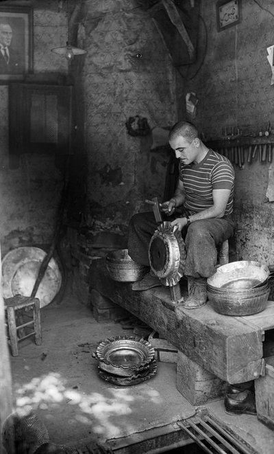 İtalyan metal işçisi, yükseltilmiş bir kap veya çömlek yapmak için bir metal levha üzerine çekiçle vuruyor, İtalya by Bernard F. Rogers