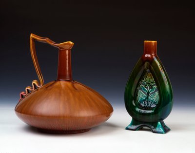 Çizgili karamel, yeşil ve koyu kırmızı sırlı, sıkıştırılmış küresel formda bir Linthorpe çömlek sürahisi ve deldi çiçek tomurcuğu süslemeli ve benekli yeşil, mavi ve kahverengi sırlı bir Linthorpe Çömlek vazosu by Christopher Dresser