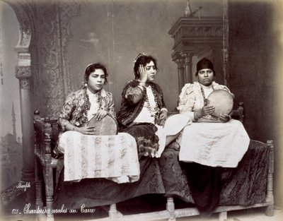 Uzun kolyeli etnik elbiseli üç genç Arap şarkıcının portresi. Stüdyoda oturmuş poz veriyorlar. İkisi bir tef tutuyor by Félix Bonfils