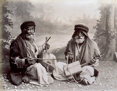 Mütevazı etnik elbiseli iki Arap müzisyenin portresi. Yaşlı adamlar yerde oturmuş stüdyoda poz veriyorlar. Arkalarında ormanlık bir manzara fonu var. by Félix Bonfils