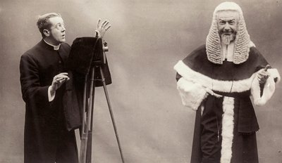 Cüppe giymiş bir adam kamerasının merceğini papa gibi giyinmiş bir adama doğrultuyor. by Rotary Photographic Co Ltd