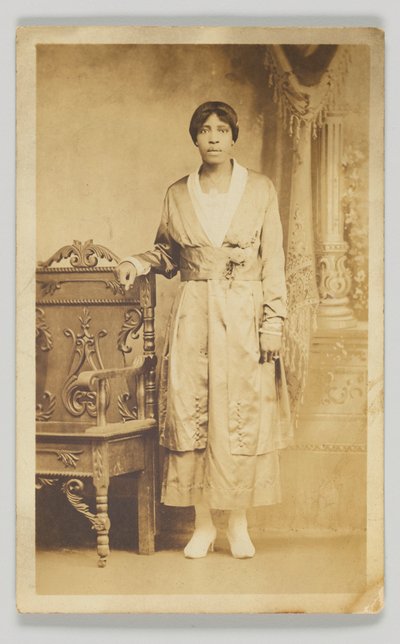 Ahşap bir sandalyenin yanında duran bir kadının fotoğrafik kartpostalı, 1904-1918. by Unbekannt