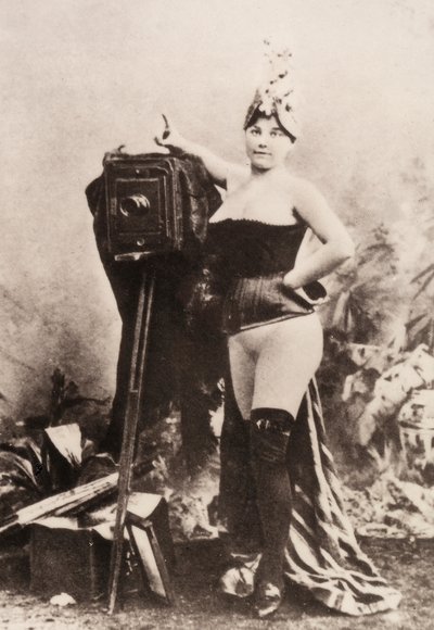 Antika bir fotoğraf makinesine yaslanmış, kısmen çıplak bir kadın portresi. by Unknown photographer