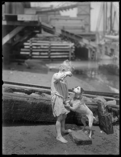 Çıplak ayaklı çocuk, muhtemelen William Gray Hassler, bir nehir veya gölün kıyısında köpekle oynuyor, New York, 1910 dolayları by William Davis Hassler